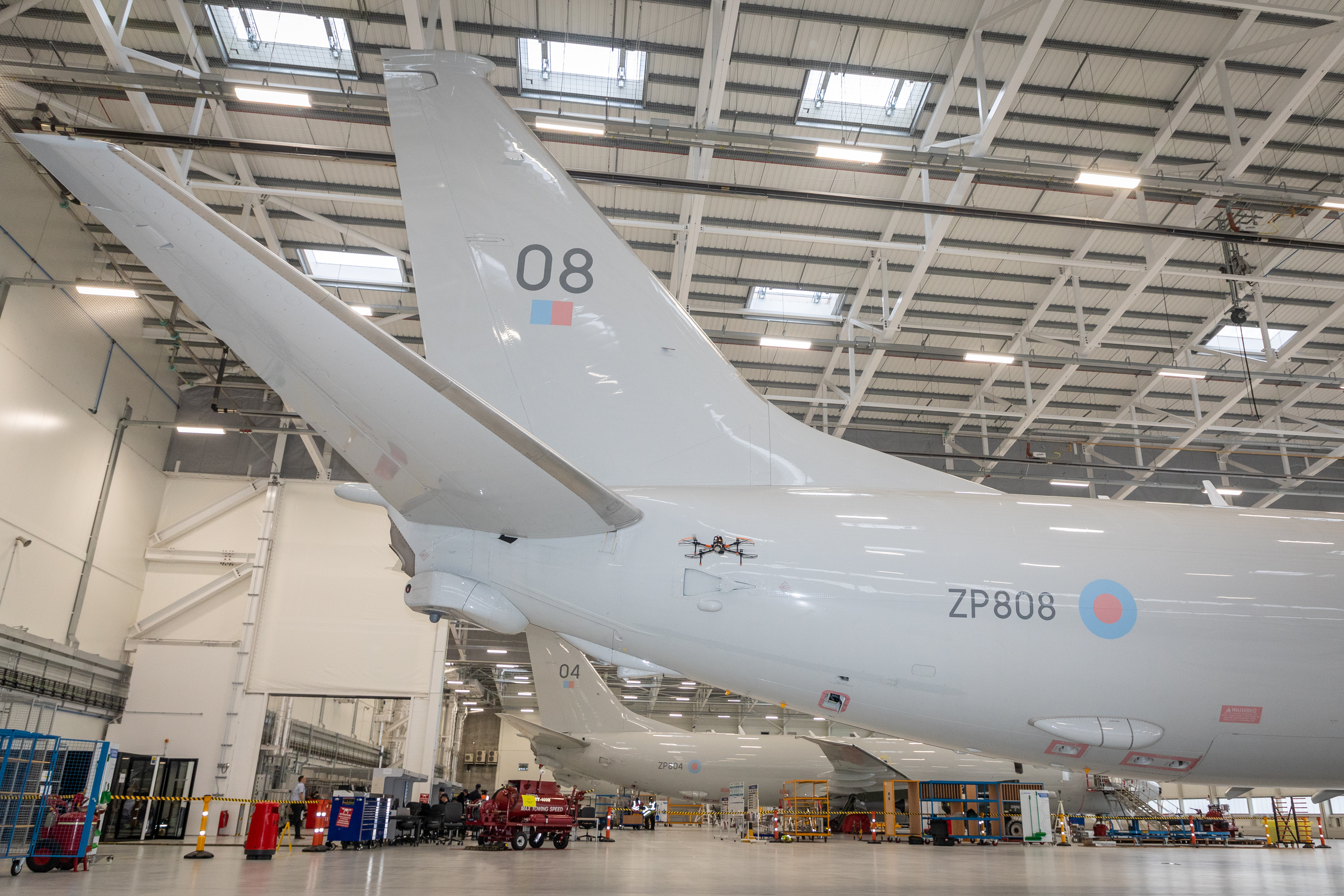 A drone flies along the side of a large aeroplane in a hangar